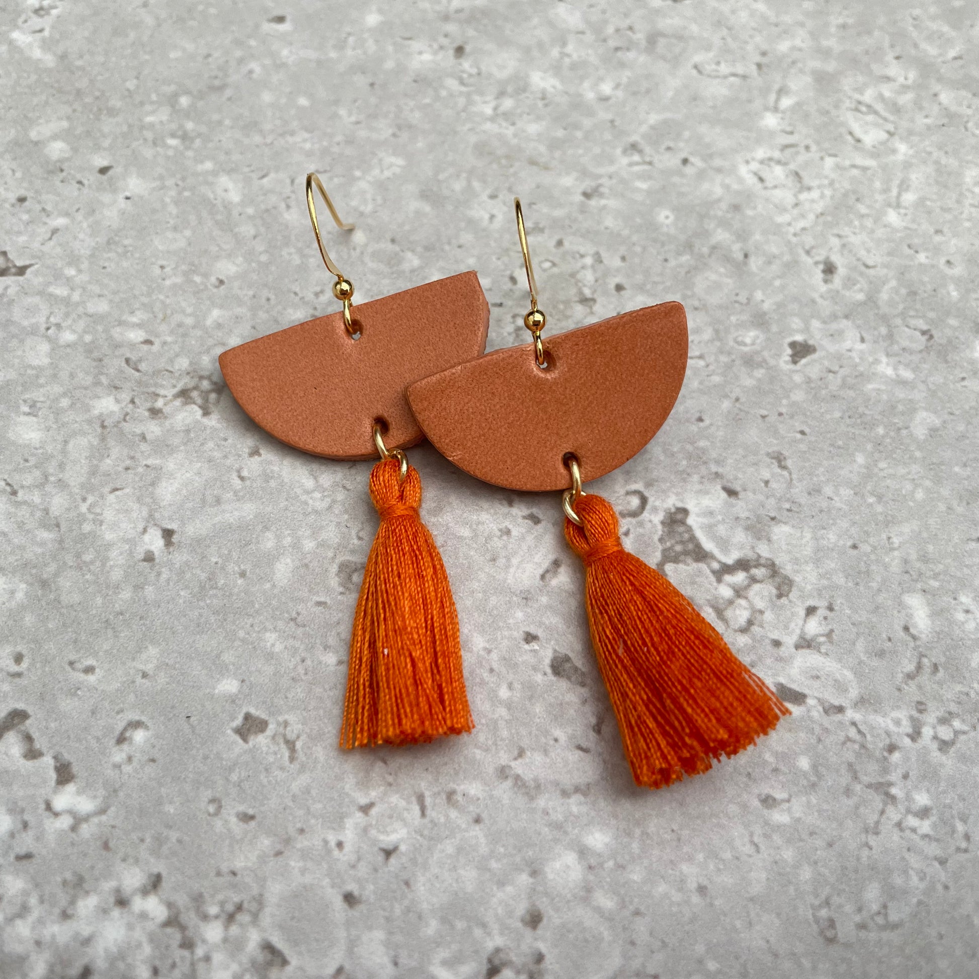 Earrings: Leather halfmoon  with cinnamon coloured cotton tassel. Gold plated hook style earring fitting.